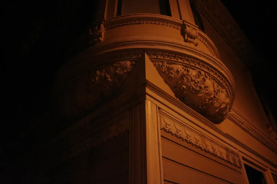 The rounded corner of an old building glowing orange at night.