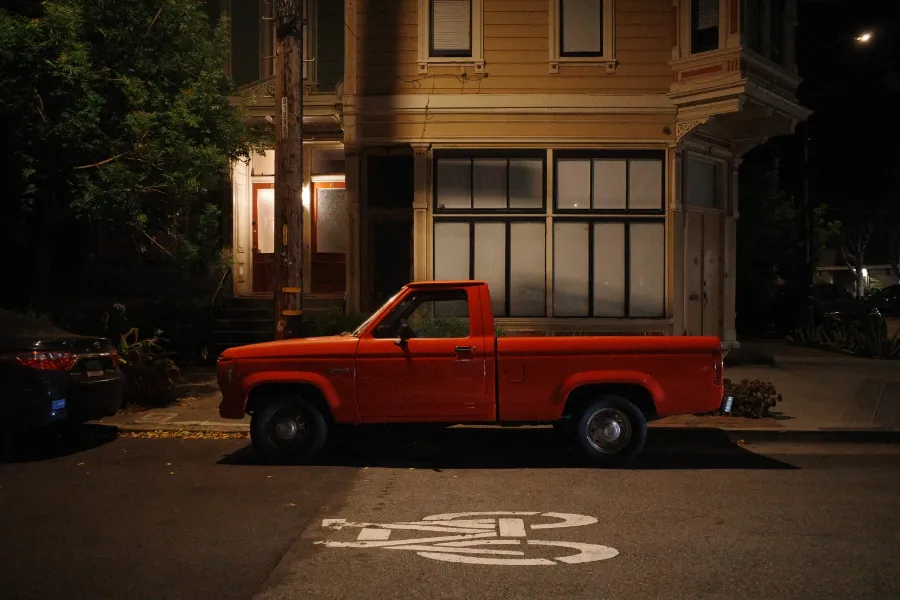A red pickup truck parked in front of a lit house at night.